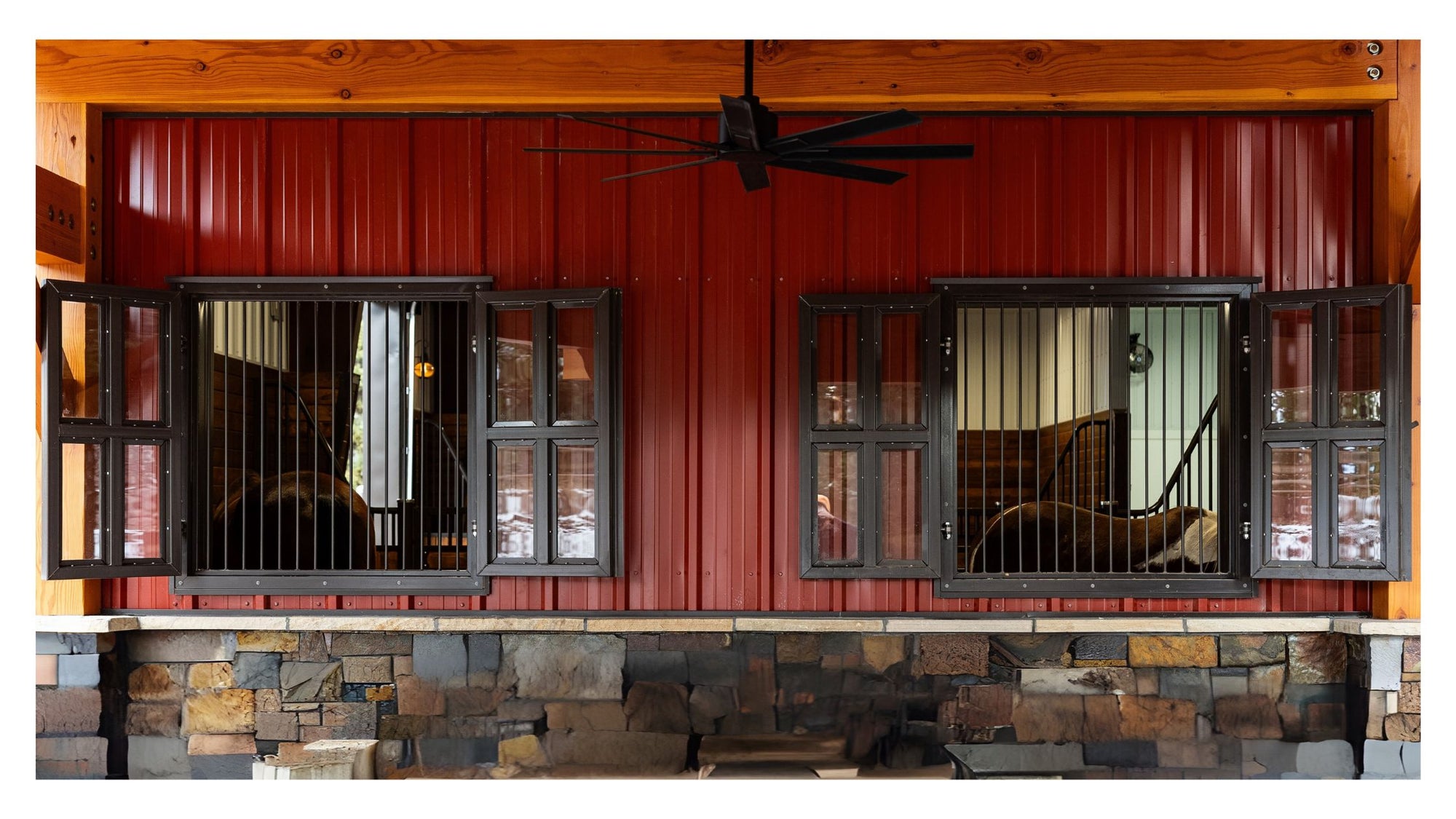 Red wooden wall with black-framed windows and stone base. Quad Fill Glass Shutter Window with Grill Guard.