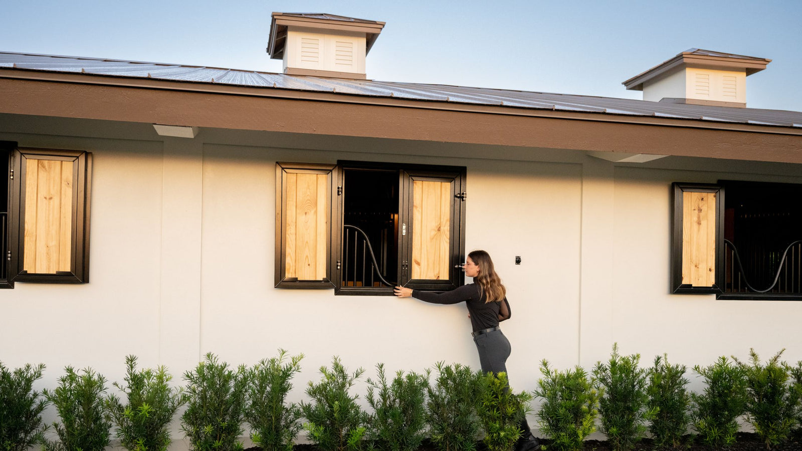 Woman standing outside the barn by the Window. Opening the Shutter Window. Hinge Vertical Lumber Fill shutters with Grill Yoke.